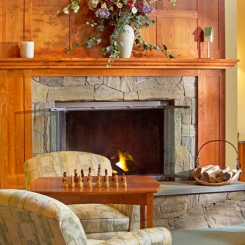 Two chairs and table with chessboard in front of fireplace and mantle with flowers in Ogunquit, ME