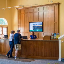 Two people at reception desk checking in with receptionist in front of TV in Ogunquit, ME