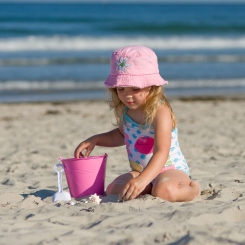 Child with pink hat playing on beach with pink bucket in front of ocean in Ogunquit, ME