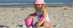 Child with pink hat playing on beach with pink bucket in front of ocean in Ogunquit, ME
